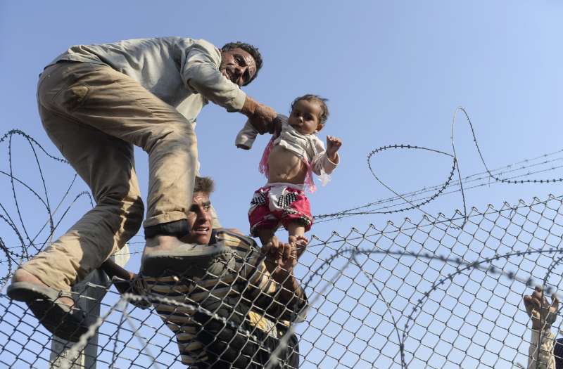 A child fleeing war in Syria is lifted over a border fence at [&hellip;]