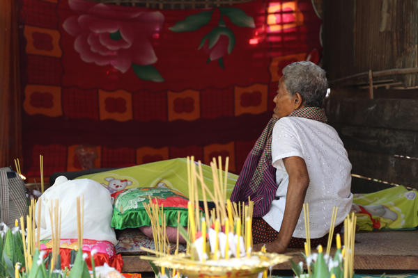 A relative sits by the covered body of Nach Ros, the fifth villager to die of HIV/AIDS in Roka commune in western Cambodia's Battambang province, Feb. 25, 2015.