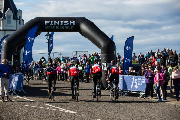 A group of Vodafone Foundation bike riders cross the finish line from the bike ride.