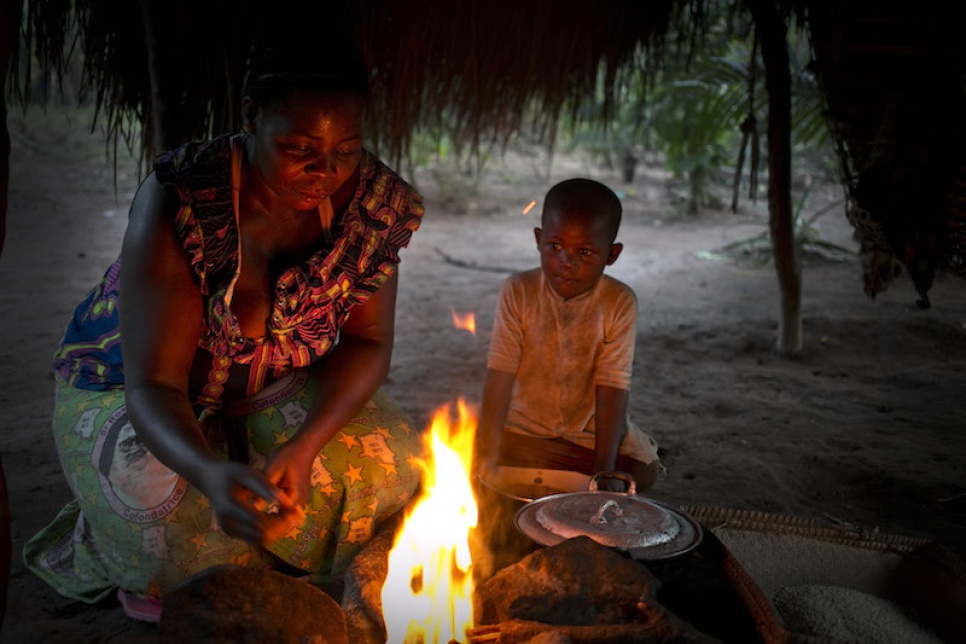 As one of her young sons looks on, Pascaline lights a fire so she can cook an evening meal for her family at their home in Dungu.
