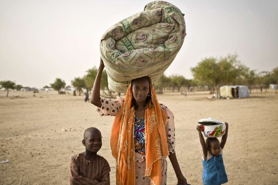 Zara, 26, her son Ousseini, 8, and her daughter Aicha, 4, carry belongings to the site where her husband Bala has started to build up their new shelter in Sayam Forage refugee camp.