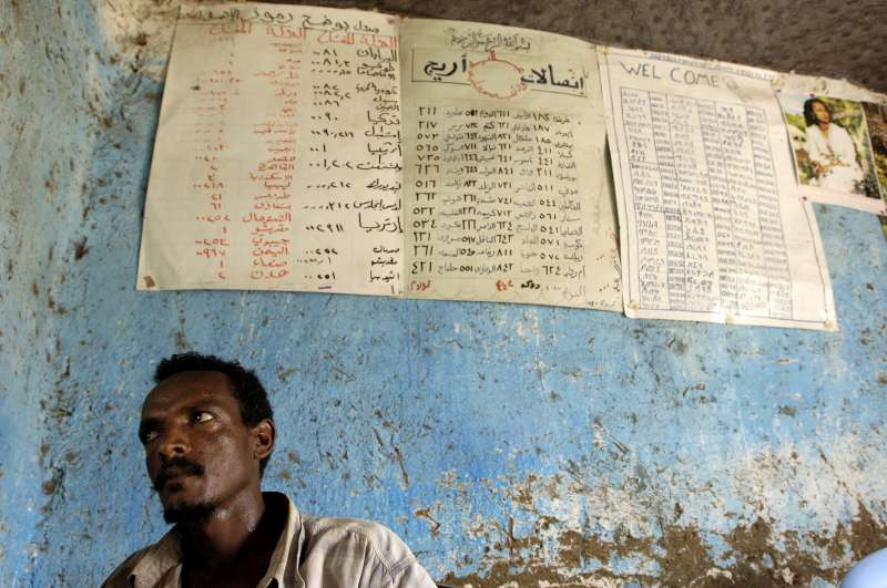 An Eritrean refugee waits to make a call at a telephone bureau in Kilo 26 refugee camp. On the wall behind him are the call rates for countries around the world. 