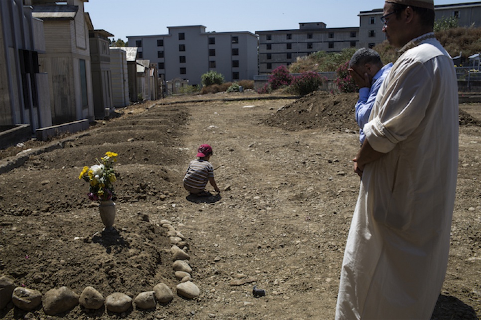 Lyad plays in front of his grandmother's grave at a cemetery in Catania, Italy, while the Imam prays nearby.