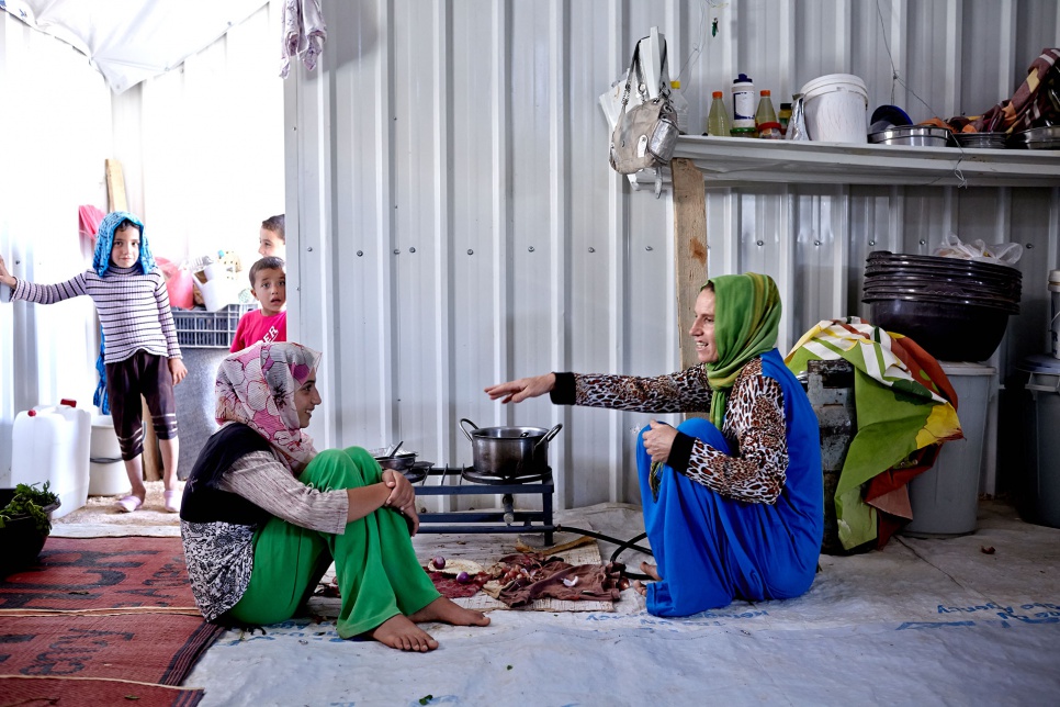 As children look on, Amer's sister, Bushra (left), and mother, Mona (right), prepare a meal in their shelter at Azraq camp in Jordan.