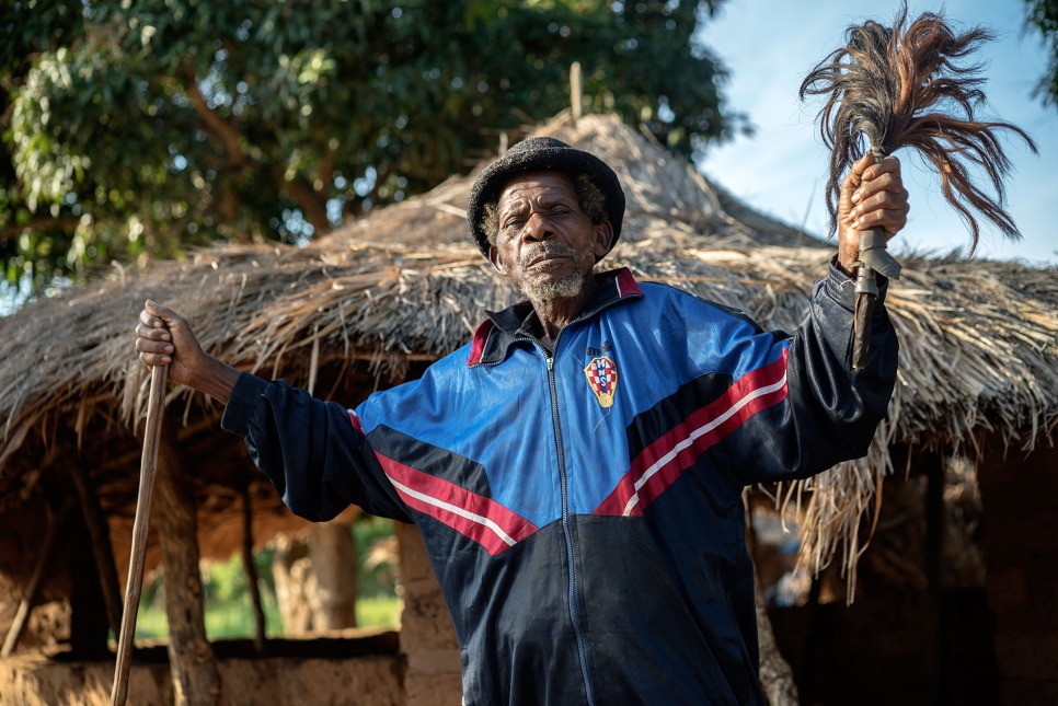 Step 2: Get the Local Chief on Board. Chief Kabwa Asumani, 84, poses for a portrait with his staff in front of the communal meeting hut in Lukwangulo, DRC.