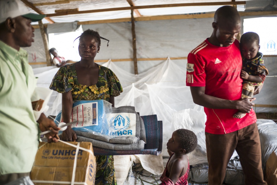 Souzane collects sleeping mats, blankets and a mosquito net at Bili camp while her husband carries their youngest child and a sibling looks on.