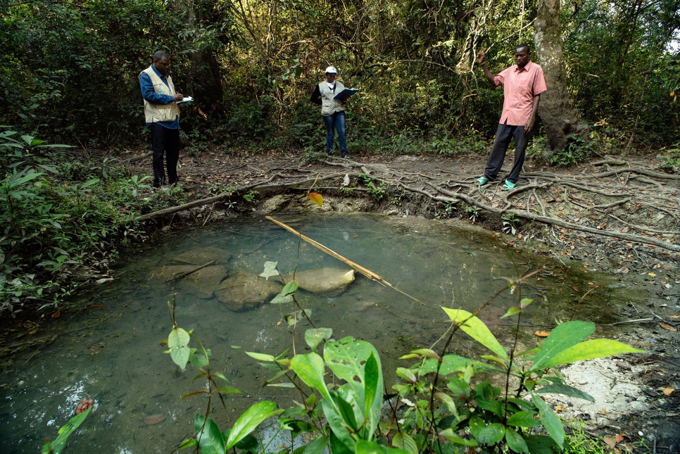 Abdou Savadogo (left), a UNHCR's water and sanitation expert, examines a seasonal water source in Dula, DRC.
