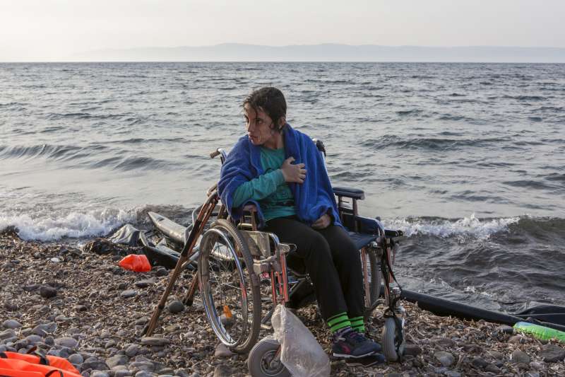 Syrian refugee Nogeen, 16, waits to be carried from the shoreline to the road after landing on the Greek island of Lesvos with her older sister Nisreen. They fled Aleppo with their parents over two years ago and had been living in Turkey before deciding to seek better medical care for Nogeen in Europe. After a very rough crossing, which left most of the passengers cold and terrified, Nogeen seemed calm and happy. Speaking fluent English, she described the journey: "I enjoyed it. I have never been on a boat before. It was very beautiful. I didn't know if I was going to live or die, but thanks to God we are here." 