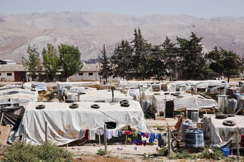  صورة للمخيم العشوائي في قرية الدلهمية حيث تعيش أسرة آية. يقع المخيم في وادي البقاع وتظهر التلال القاحلة خلف الصورة. يضم المخيم 128 مأوى لما يزيد عن 1,000 شخص. ​