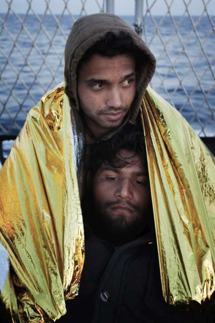 شابان يتشاركان بطانية حرارية للتدفئة بعدما تم إنقاذهما أثناء محاولتهما عبور البحر المتوسط من ليبيا.