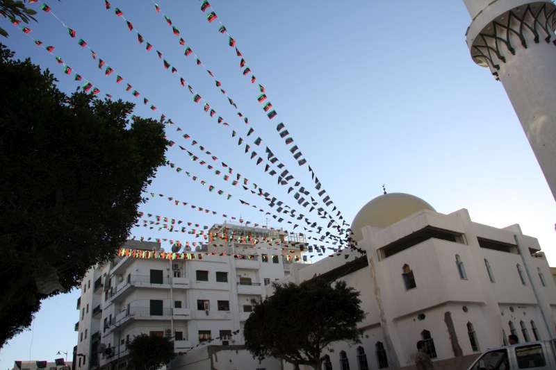 حبال مزدانة بعلم ليبيا الجديد ترفرف من أحد المساجد في طرابلس بعد عام من ثورة الشعب ضد النظام السابق. ولكن العديد من النازحين الداخليين لم يحتفلوا.