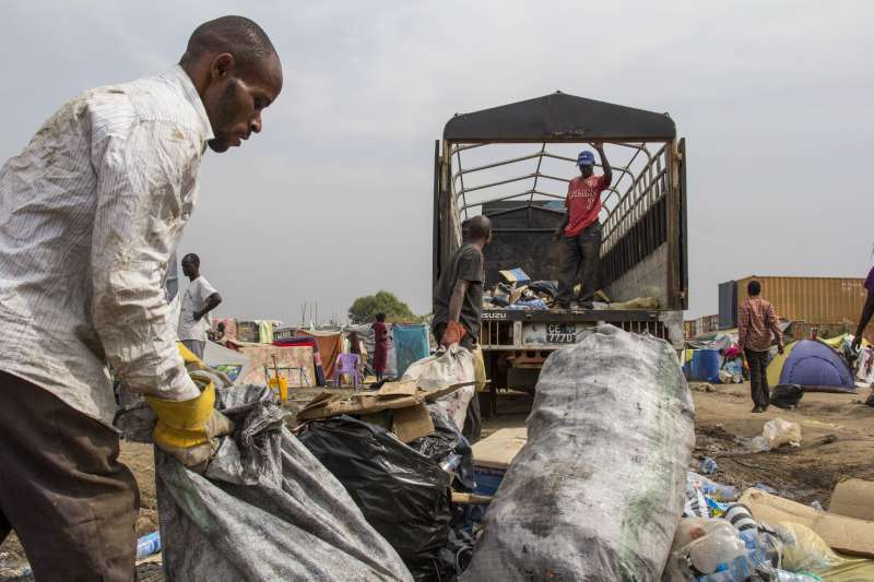 عاملون يقومون بإزالة أكوام القمامة التي جمعها الأشخاص النازحون من المجمَّع. ويشكل الحفاظ على نظافة المخيم المؤقت المكتظ تحدياً كبيراً. 