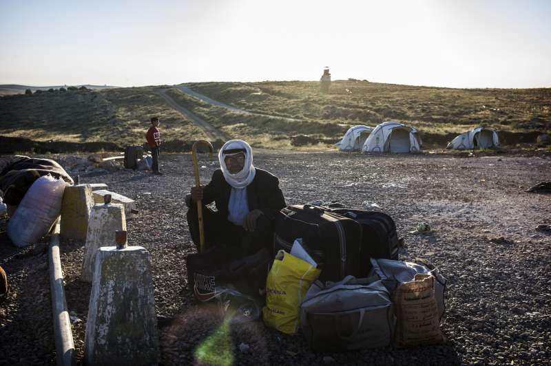 A Syrian refugee stops and rests with his belongings at the end of his journey from Syria.  He has just crossed the border, which can be seen behind him.