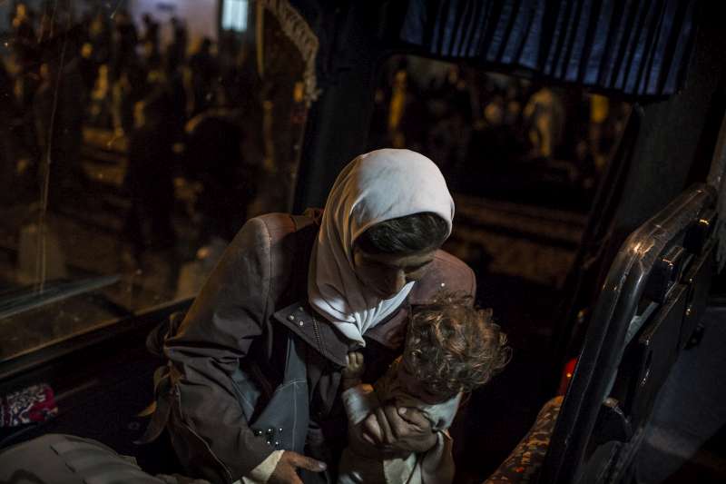 A newly arrived Syrian refugee woman carries her child as she boards the bus that will take her to Za'atri.