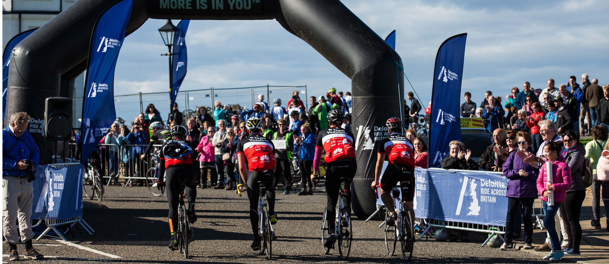 A group of Vodafone Foundation bike riders cross the finish line from the bike ride.