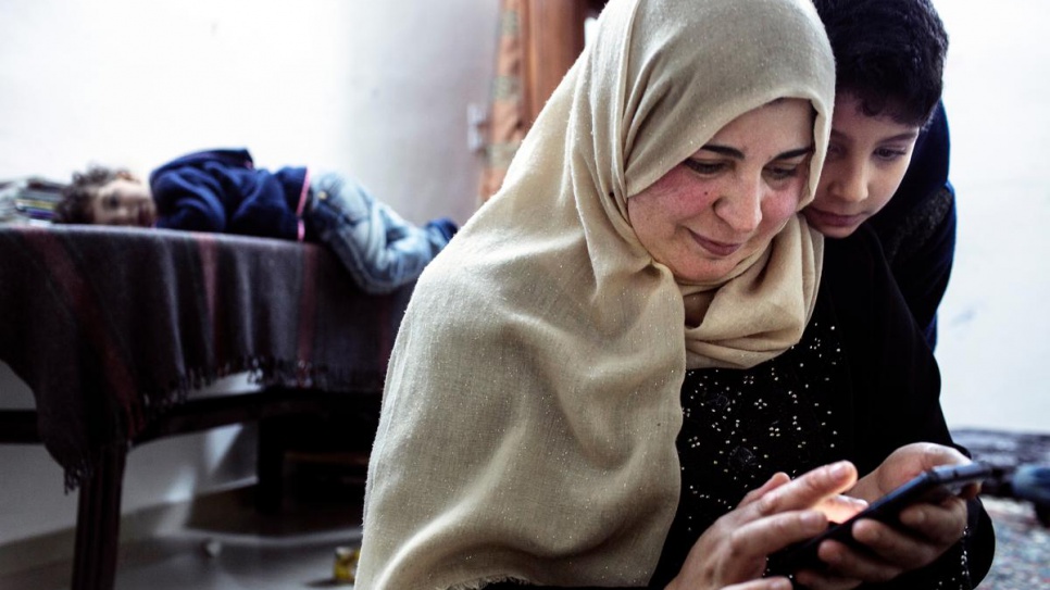 Syrian refugee Bushra sits with her children in Jordan in 2015, showing them images and text messages from their father, who left months earlier for Europe.