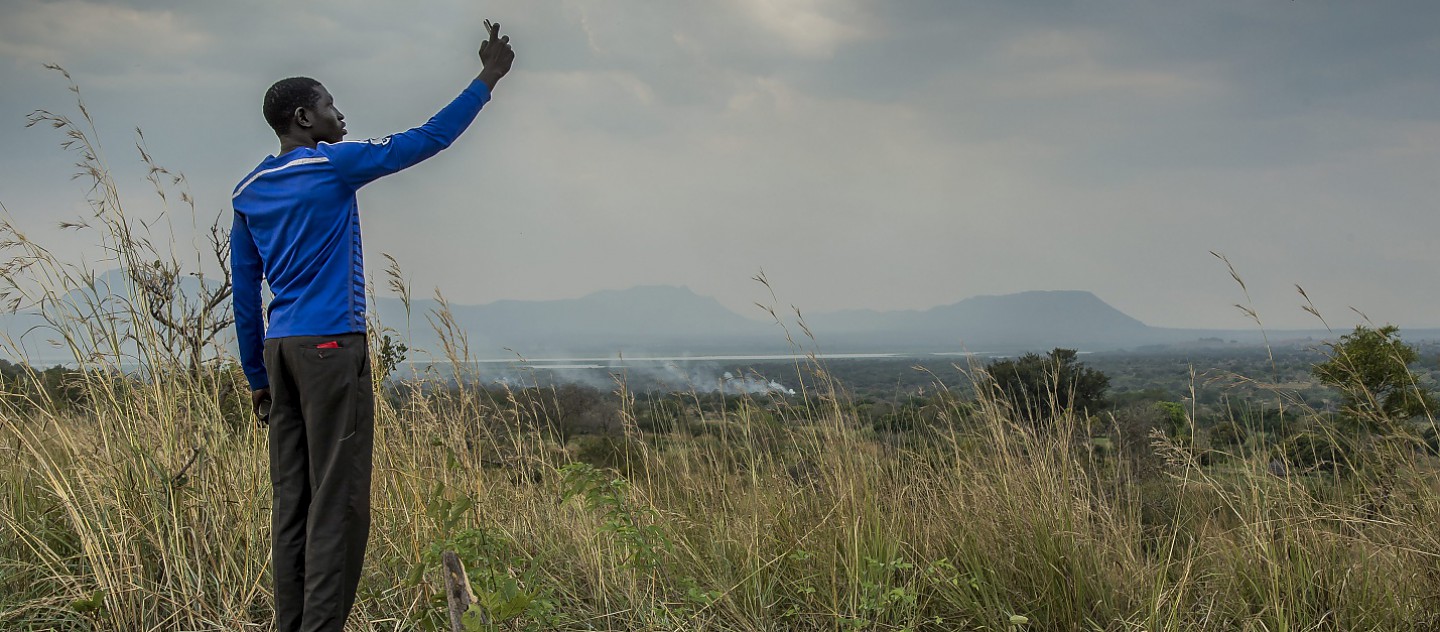 A young South Sudanese man tries to get signal on his mobile phone in Nyumanzi refugee settlement, Adjumani, northern Uganda. From this hill overlooking the refugee settlements, refugees can sometimes pick up the South Sudanese phone network and make cheaper calls home. 