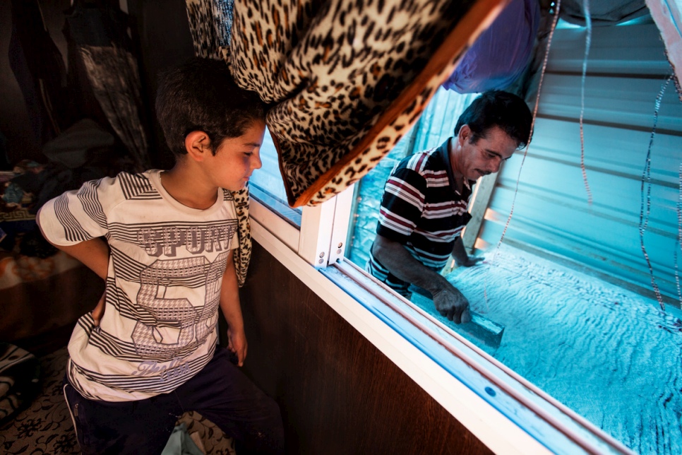 Faris watches from the bedroom as his father Abu Rabee' cuts "raha" into small pieces at his caravan at Za'atari refugee camp.