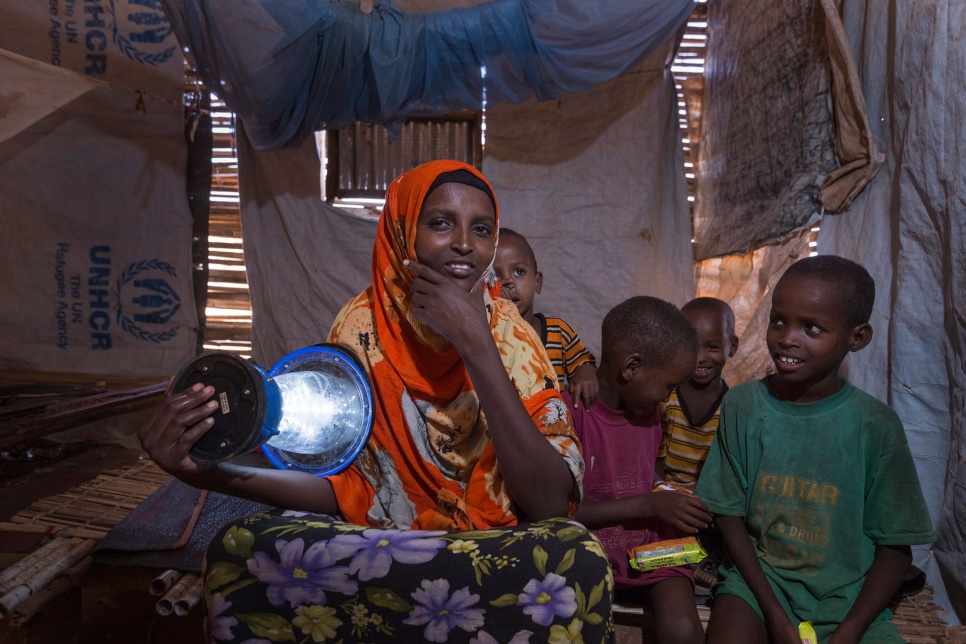 Joined by her children, Kadija, a refugee from Somalia, holds an Ikea solar lamp inside her house in Ethiopia's Dollo Ado camp.