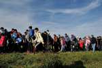 A column of refugees and migrants is walked across fields by police in...