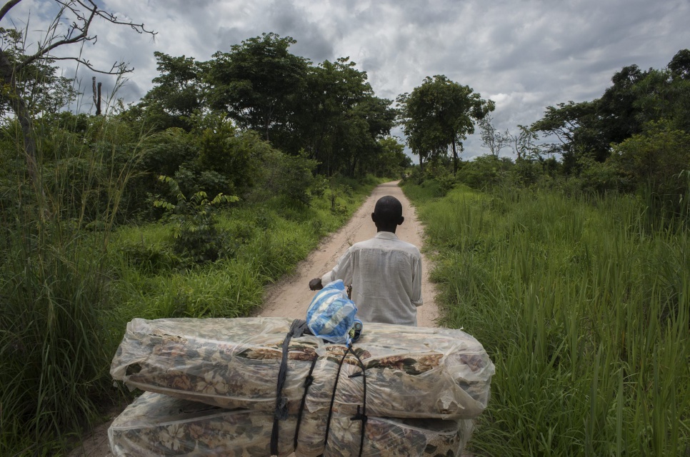 Vincent pushes a bicycle carrying his mattress along the road in Katanga Province. He fled from Kamala to Manono following clashes and is among the first residents to return.