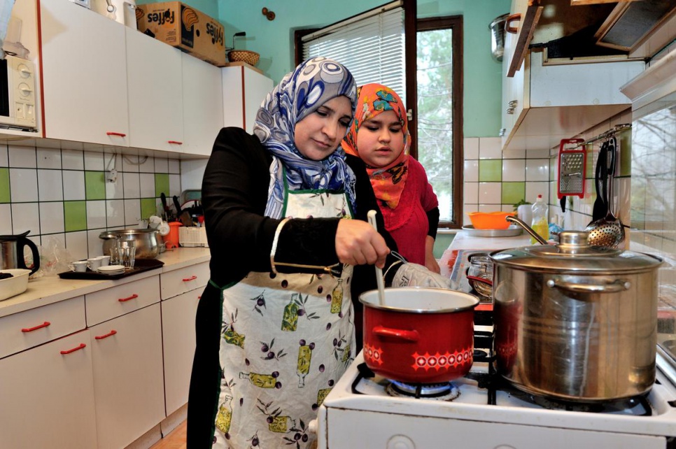 Izdihar cooks dinner for her family with the help of her 13-year-old daughter Samira in the kitchen of their new home.