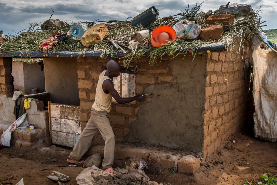 A newly arrived refugee renders the walls of his home in Kashojwa. Many refugees choose to use grass and other items to help waterproof the roofs.