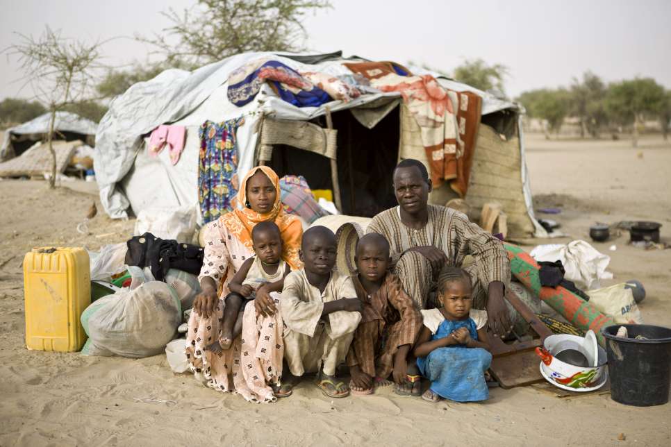 Bala pose avec sa femme et leurs enfants, devant un abri temporaire, qu'ils ont obtenu à leur arrivée au camp de réfugiés du sud du Niger. 