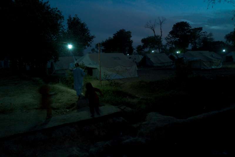 JALALA, PAKISTAN- MAI 2009
A la lumière des ampoules, deux jeunes filles se dépêchent de regagner leur tente à la tombée de la nuit dans le camp de personnes déplacées de Jalala. Le camp accueille temporairement des milliers de réfugiés de Swat et de Buner qui ont fui les combats qui faisaient rage alors que l'armée pakistanaise délogeait les insurgés talibans. 
