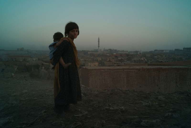 LAHORE, PAKISTAN- NOVEMBRE 2009 
Couverte de saleté, une jeune fille afghane ramène son petit frère au camp de réfugiés de Sagiam Pull qui est situé au bord de la décharge. Les enfants réfugiés afghans commencent à travailler à tout juste quatre ans en fouillant les ordures. Ceux qui travaillent dans la décharge sont souvent obligés de survivre en mangeant les déchets qu'ils trouvent. 

