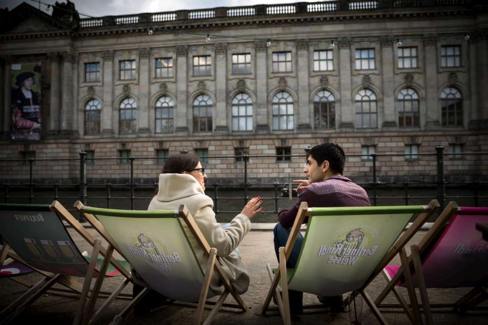 Syrian refugee Fahed and German consultant Anne-Marie sit outside a beach bar by the river.