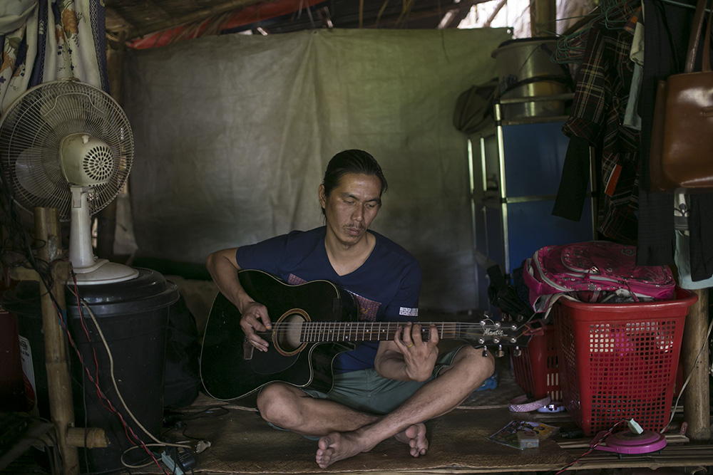 La Htaw Zau Pan plays the guitar in his family's shelter