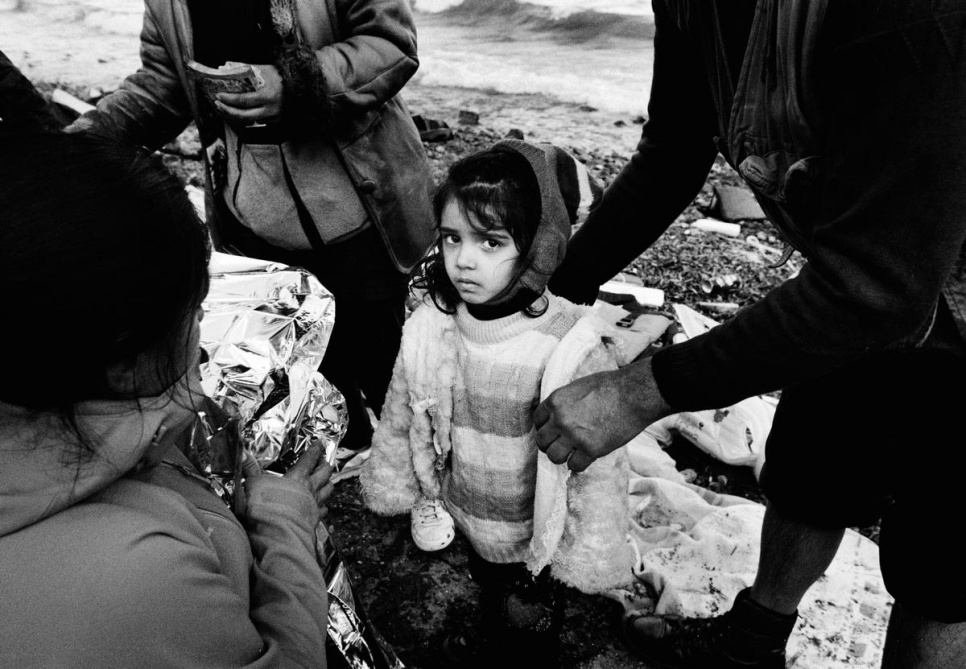 Volunteers prepare to wrap a young girl in an emergency blanket to protect her from the cold wind.