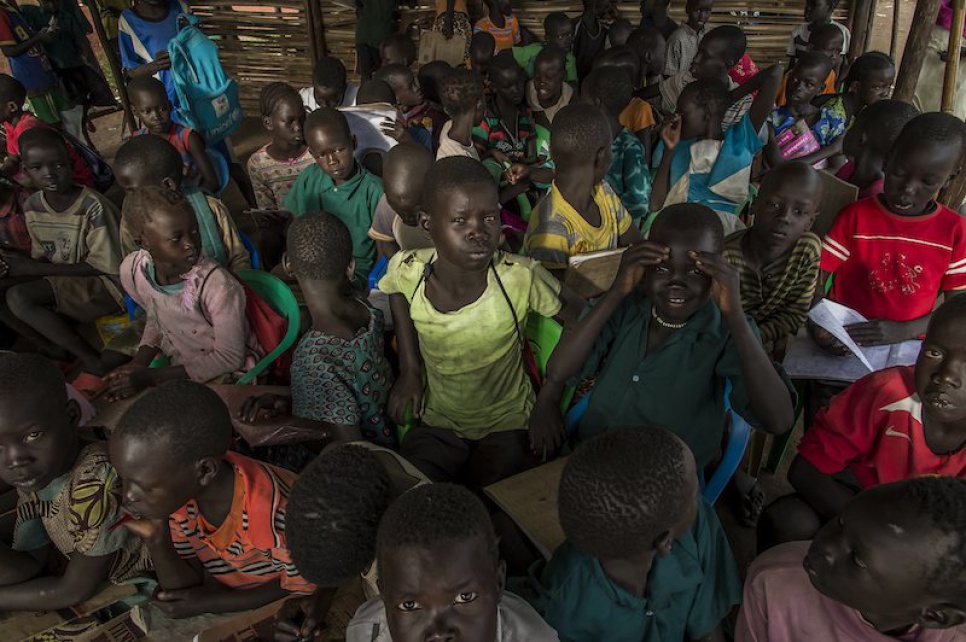 Eager to attend Alaak's science lesson, refugee children squeeze into a makeshift classroom, sometimes using upturned food cans as chairs.