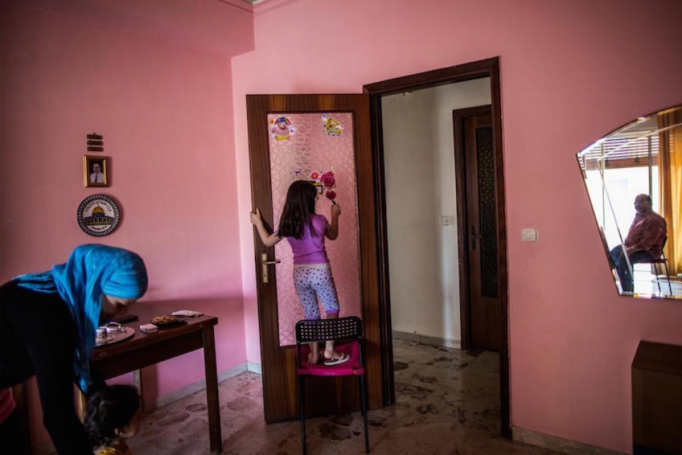 Alberto and his wife Muna sit together at home, while their children play in the living room.