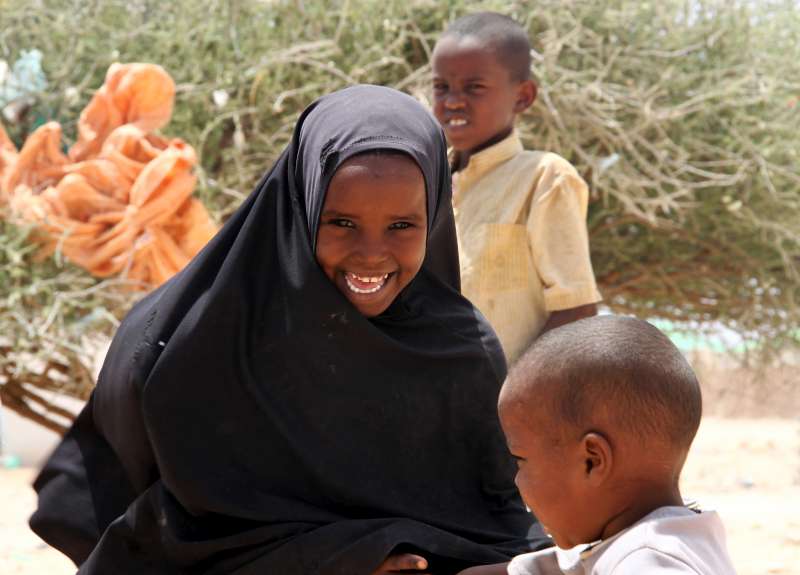 A smiling IDP girl plays with her younger brother at the Halabokhad settlement in Galkayo, Somalia. Decades of civil war and famine have robbed children of a permanent place to call home. 