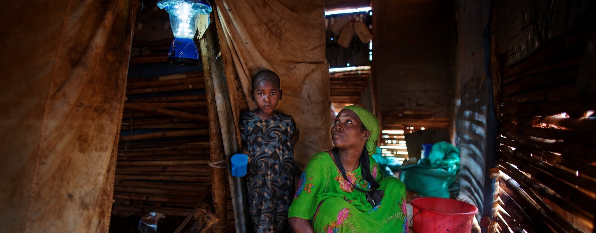 Refugee mother and her son in a shelter lit by one of UNHCR's solar lights.