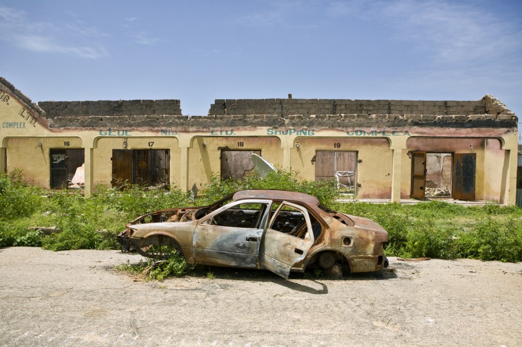 A burned out car lies in a street of destroyed homes in Gwoza, recently liberated by Nigerian armed forces.  Insurgents destroyed most of the city before they left, such as this shopping center, and burned cars. © UNHCR / Helene Caux