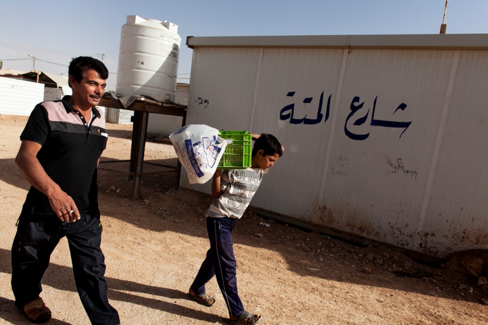 Faris helps his father, Abu Rabee', by carrying the box of "raha" sweets to the market in the main shopping street at Za'atari refugee camp.