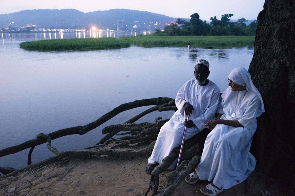 Imam Moussa Bawa and Sister Maria Concetta sit by the banks of the Oubangui river in Zongo, DRC. Across the river the lights of Bangui can be seen.