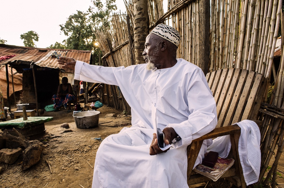 As the sun sets, Imam Moussa Bawa, 72, gestures toward his home in Zongo, Equateur Province, DRC. He was born in nearby Libenge and has lived in Zongo for 34 years.