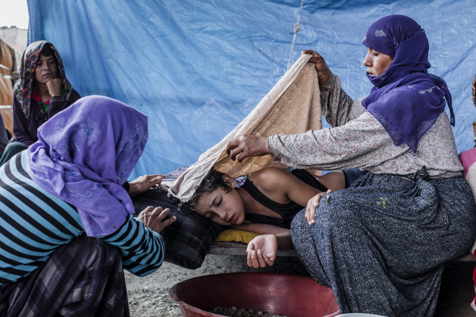 Syrian refugee Nizal, 14, is tended to by his mother (left) and a relative, after falling ill with a high fever and vomiting.