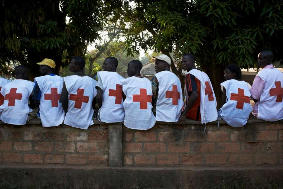 Central African Republic (CAR)/ IDPs/ Red Cross workers sit on a wall at the Bishop's residence in the town of Bossangoa on December 19, 2013. UNHCR is distributing 3000 Non Food Items (NFIs) to those in need. There are 35,500 IDPs sheltering at the residence of the Bishop and another 5000 sheltered between the home of the Imam and a local school. Many fled their homes in September when violent attacks broke out between anti-Balaka fighters and Seleka rebels. On Thursday 5th December Christian anti-Balaka militants entered the city and attacked Seleka rebels. 18 civilians were killed in Bossangoa during these attacks. The Seleka made up of a Muslim majority with many of the rebels originating from northern Central African Republic, Sudan and Chad brought to power a new president Michel Djotodia, a former Seleka leader in a March 24, 2013 coup. The political establishment has failed to control the armed group that has wreaked havoc, including murdering, looting and burning of villages on the civilian population with mass displacements resulting. / UNHCR / S. Phelps / December 2013