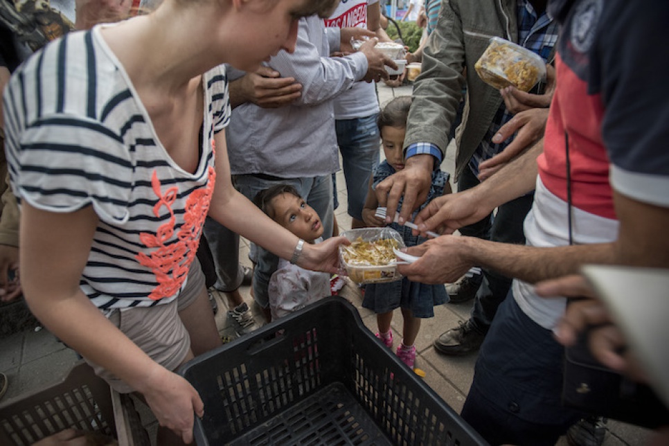 Little refugee children are at first shy to accept the plates and spoons, but when parents encourage them they reach out for the meal eagerly.