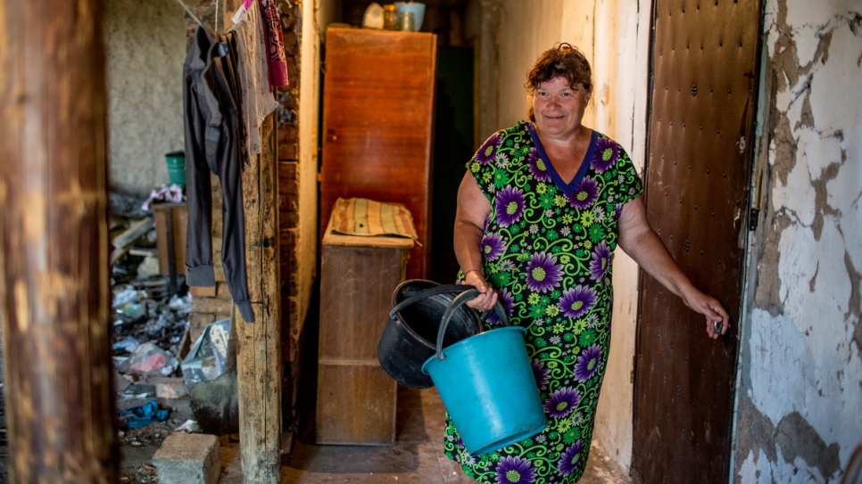 Anzhela's mother goes to get water from a neighbour. Their home in Novosvetlovka was severely damaged in the 2014 hostilities in the Luhansk region of Ukraine.