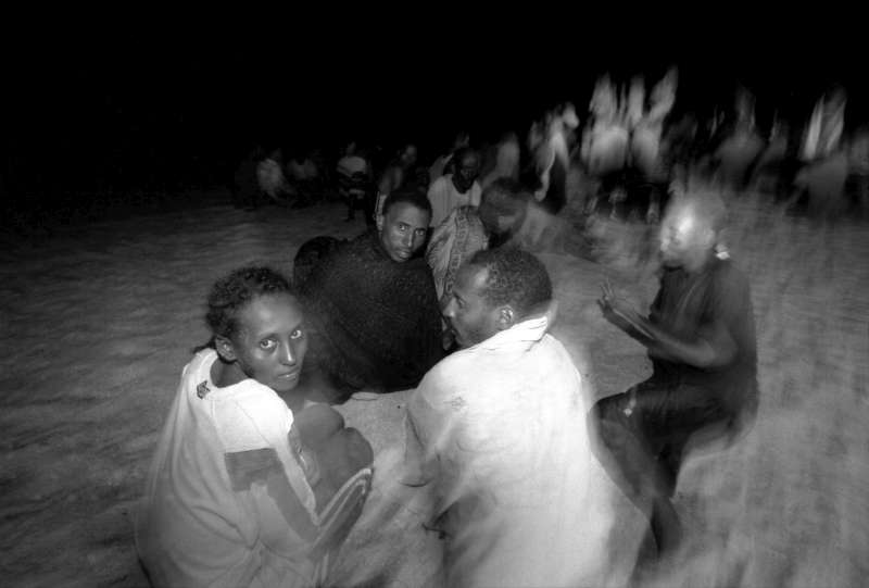 Trying to keep warm, a woman from Addis Ababa joins a group of recently arrived Ethiopians and Somalis on a beach in Yemen.