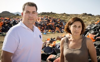 — Efi Latsoudi (right) and Konstantinos Mitrigas (left), stand next to thousands of discarded life jackets at a landfill site on Lesvos. © UNHCR /Andrew McConnell