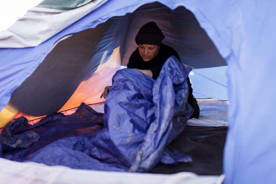 Nisrine spreads out a piece of plastic to act as insulation against the rain and cold.