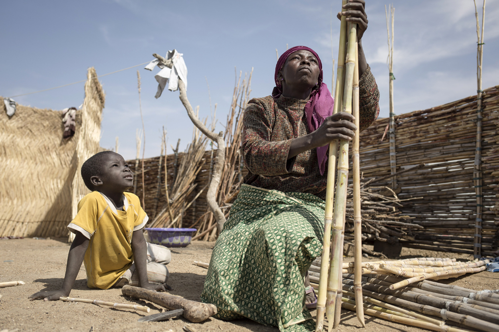 Nigerian refugee mother Rahia and her son assemble bamboo sticks to build up a fence for their home in  Minawao camp, Cameroon. They were kidnapped and held by Boko Haram for 18 months.   © UNHCR / Alexis Huguet
