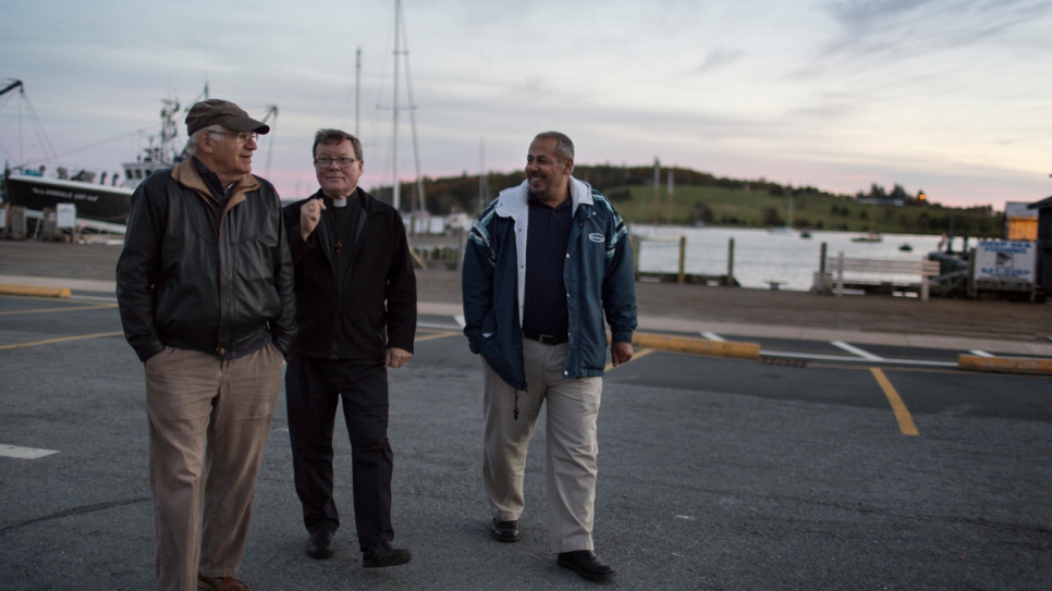 David Friendly (left) and Father Michael Mitchell spend time with Ahmad Ayash on the pier in Lunenburg.